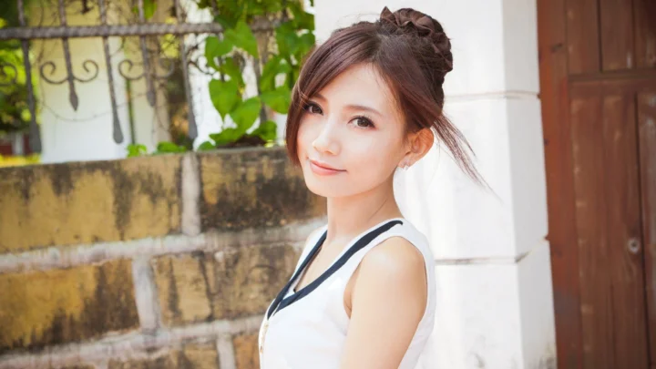 一名成年女性站在带有绿植、石墙和木门的户外建筑旁微笑看向镜头。