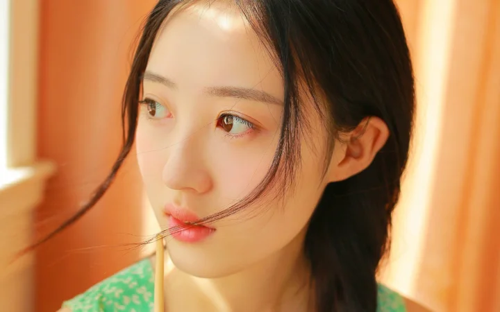따뜻한 실내 조명 아래 여성이 옆모습으로 앞을 바라보고 있다.