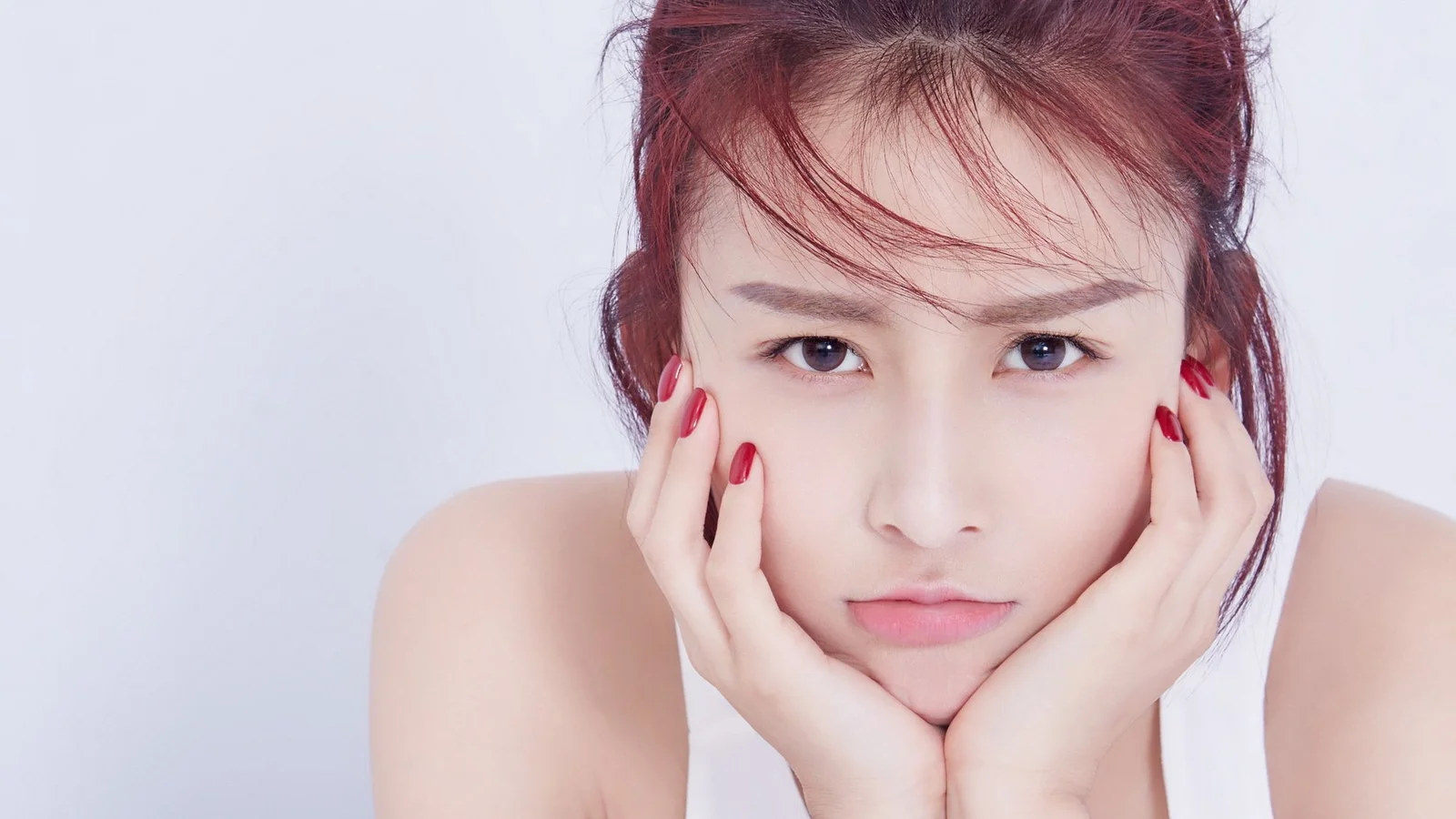 밝은 배경 앞에서 성인 여성이 양손으로 볼을 받치고 카메라를 바라보고 있습니다.