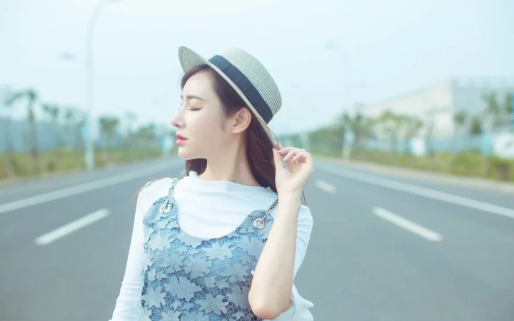 모자를 쓴 여성이 밝은 야외 풍경을 배경으로 넓은 도로 한가운데 서 있습니다.