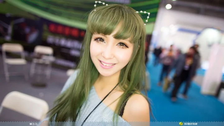一名留着长绿色头发的女性在室内展会背景前微笑看向镜头。