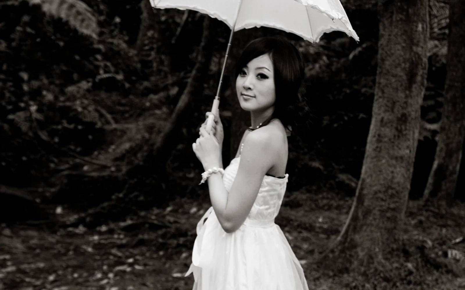 一名身穿白色连衣裙的女性在树林中撑着白色雨伞。