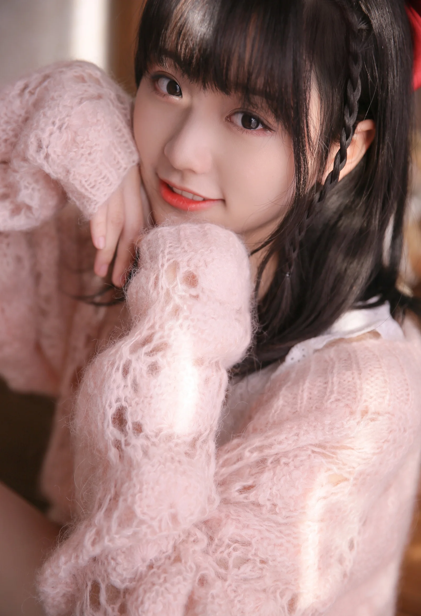 一位深色长发女性身穿蓬松的粉色毛衣，面对镜头微笑。