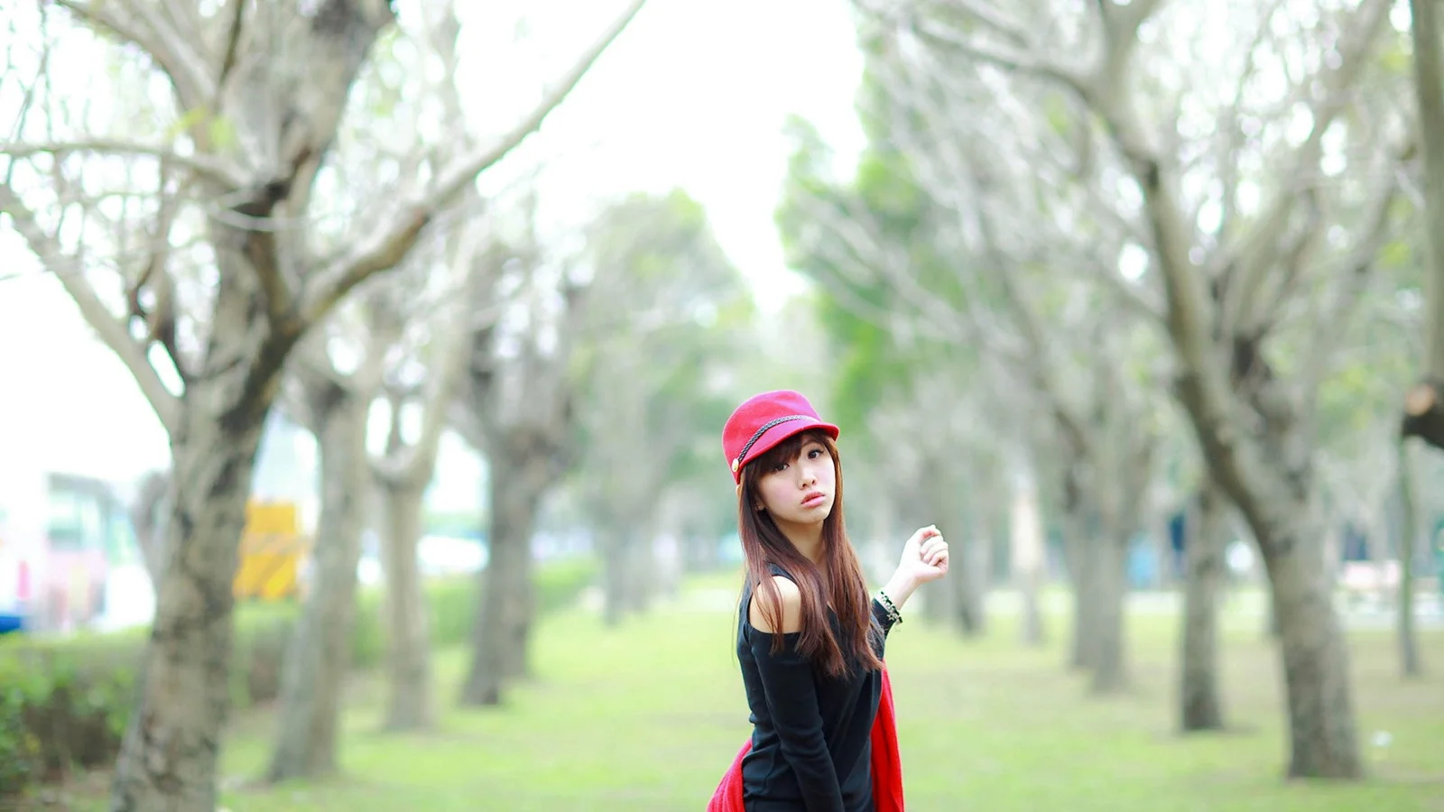 一名戴红色帽子的女子站在树木环绕的公园中。