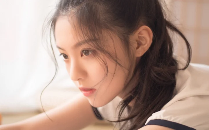 짙은 긴 머리의 여성이 부드러운 빛 속에서 옆을 바라보는 클로즈업 인물 사진입니다.