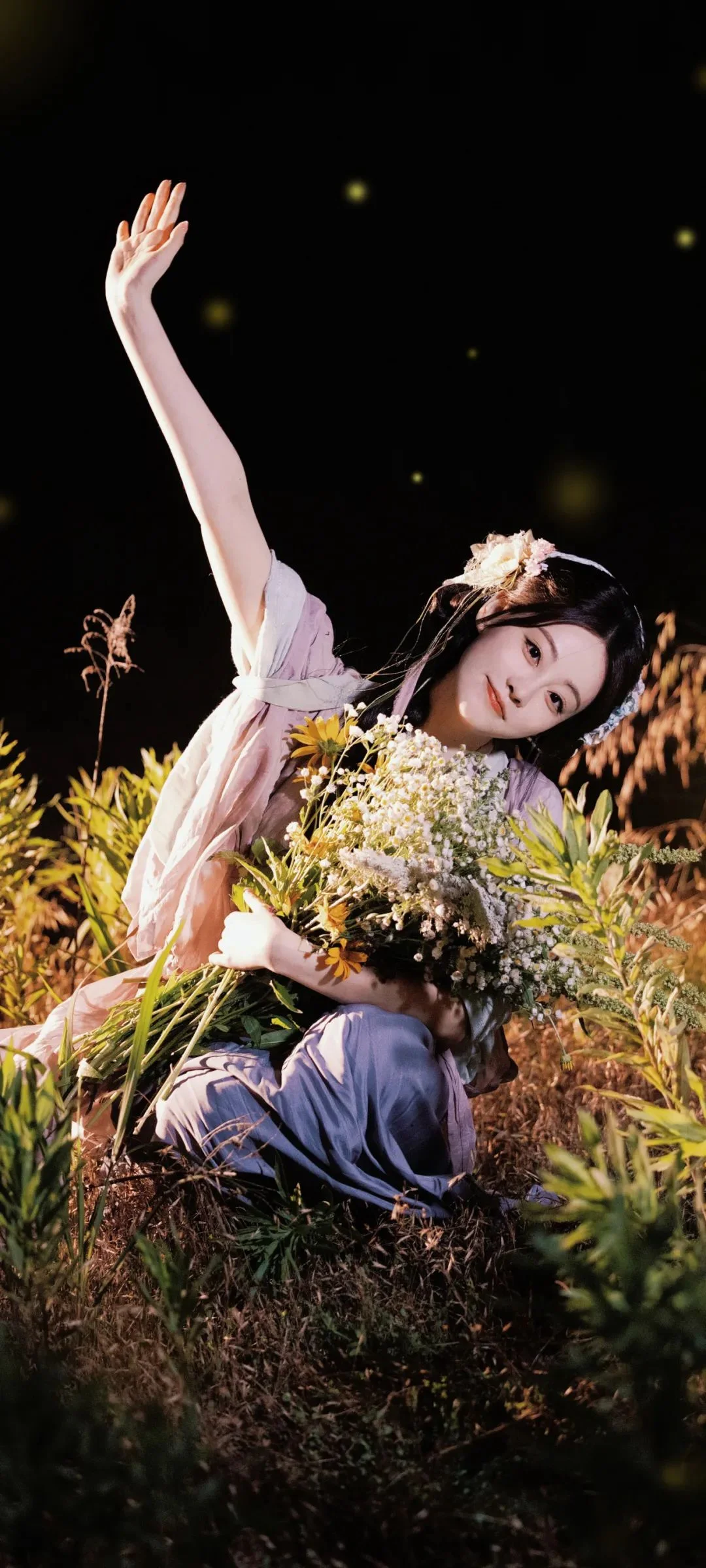 一名女性在花叢中手捧花束並抬起一隻手。