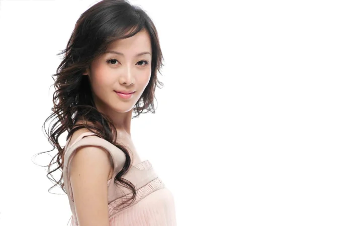 흰색 배경 앞에서 밝은 색 민소매 상의를 입은 성인 여성이 카메라를 향해 미소 짓고 있다.