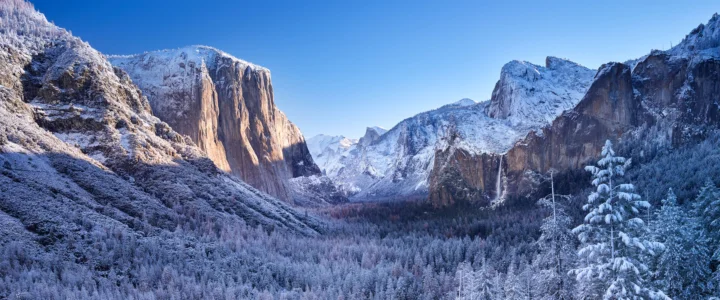 蓝天下的积雪山谷、峭壁和覆雪森林构成壮阔的冬季风景。