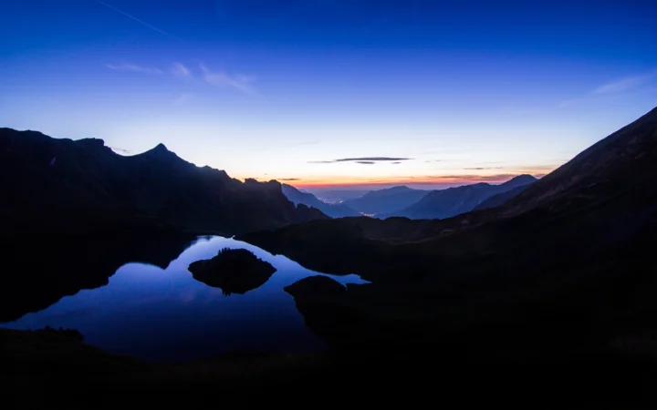 暮色中的群山环抱着一片宁静湖泊，天空映出橙紫色晚霞。