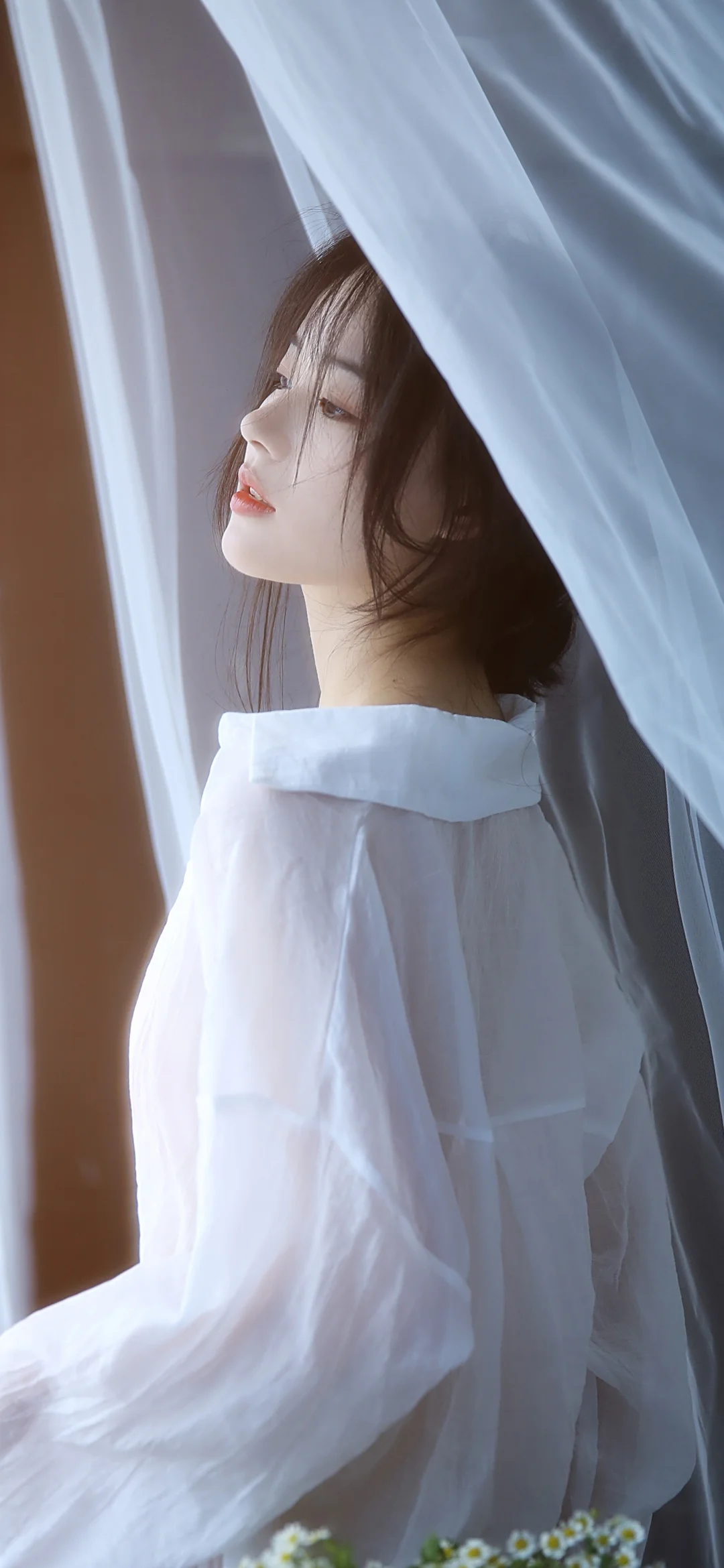 一名身穿白色上衣的女子站在半透明纱帘旁。
