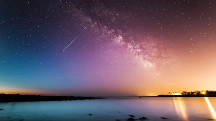 银河横跨夜空，星光映照着宁静的海面与远处灯火。