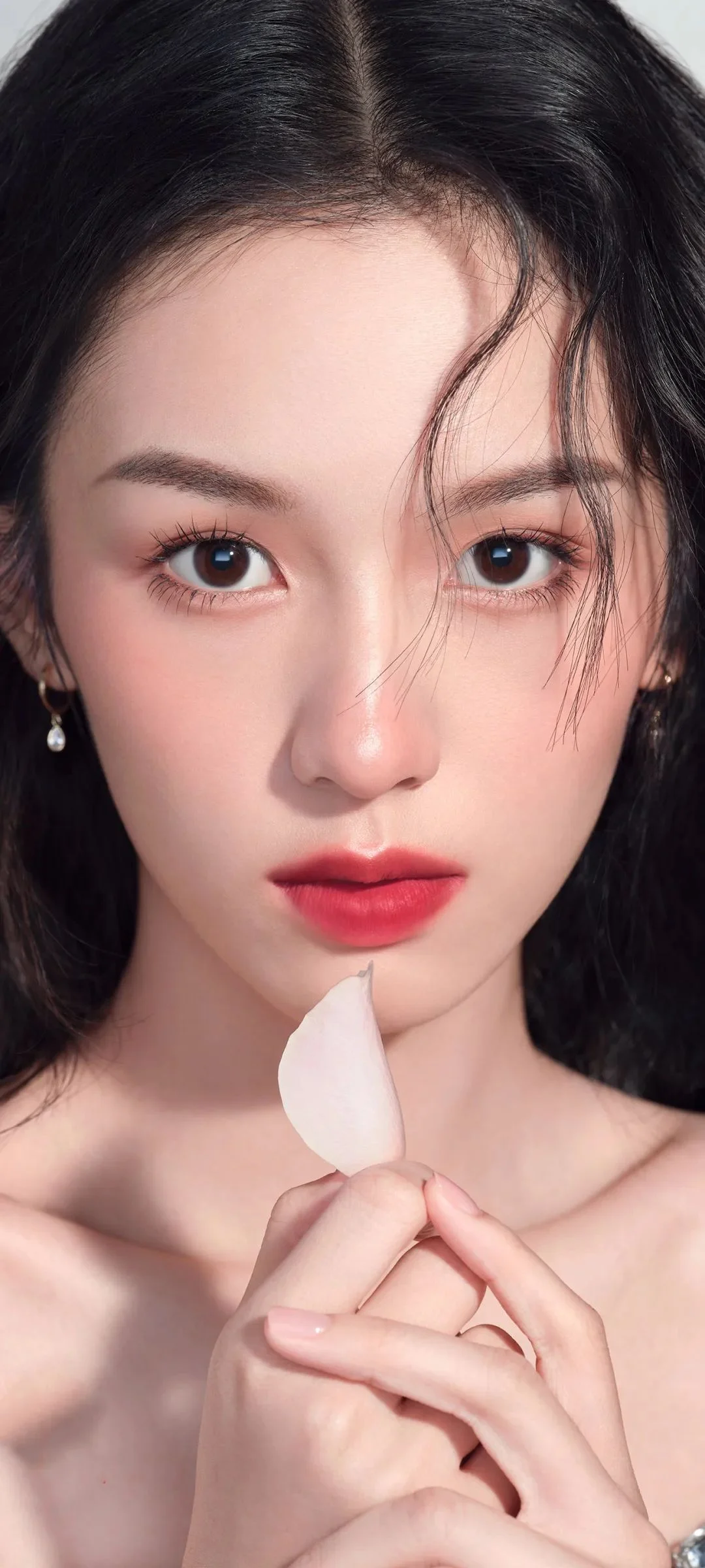 一位女性近距离注视镜头，手持一片白色花瓣靠近脸部。