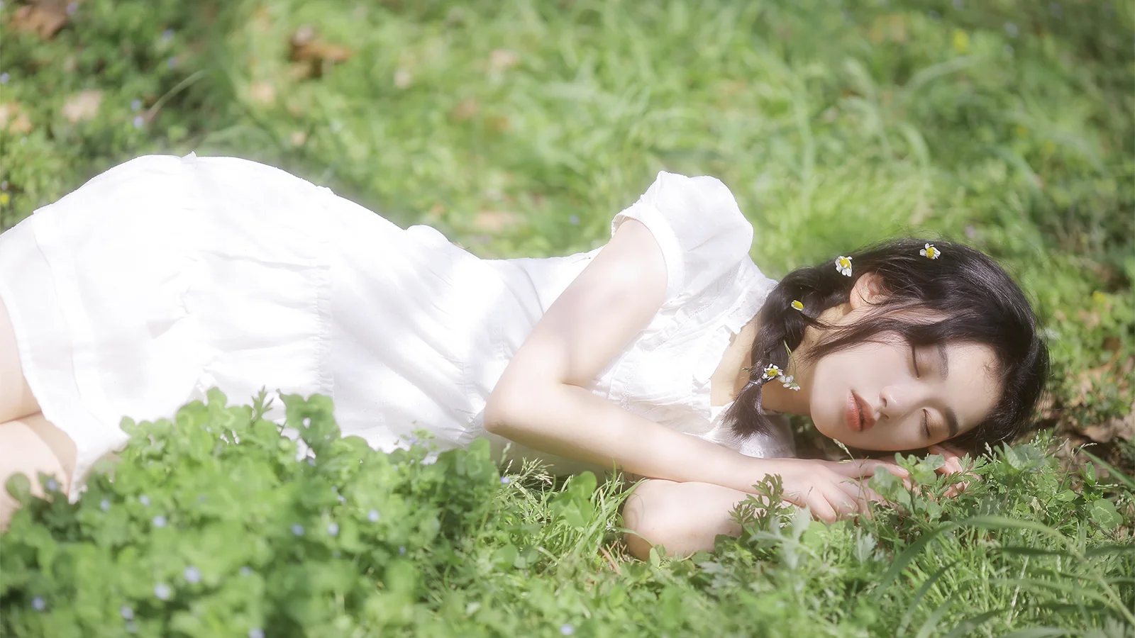 白いドレスを着た女性が、陽光の当たる草地に横たわっています。