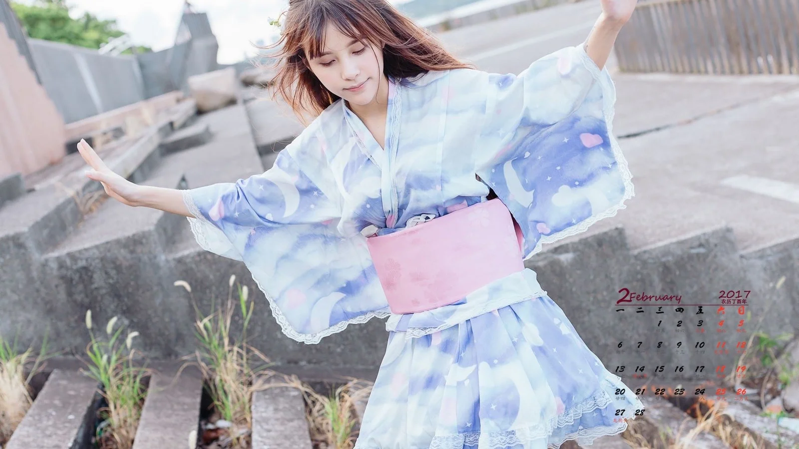 淡い青色の服とピンクのウエストバッグを身につけた女性が屋外の階段脇に立っている。