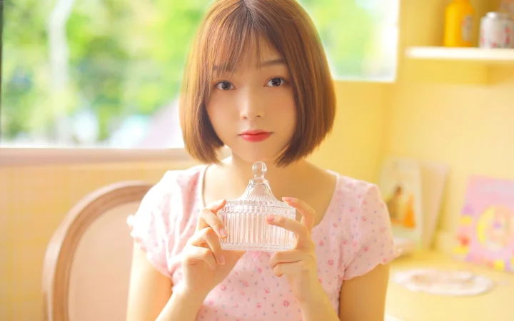 一位短发女子在明亮温暖的室内手持透明香水瓶。