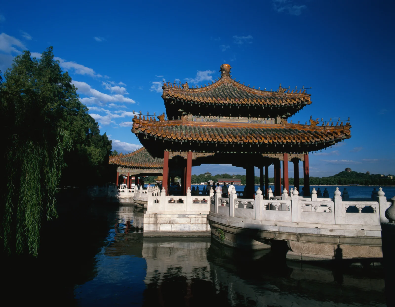 蓝天下，一座古典中式亭台横跨湖面，周围环绕着树木与倒影。