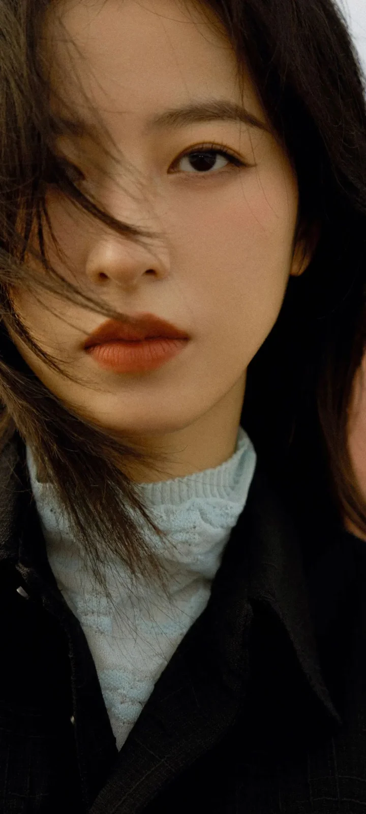一名成年女性的近距离肖像，黑发披肩，穿着深色外套和浅色高领衣物。