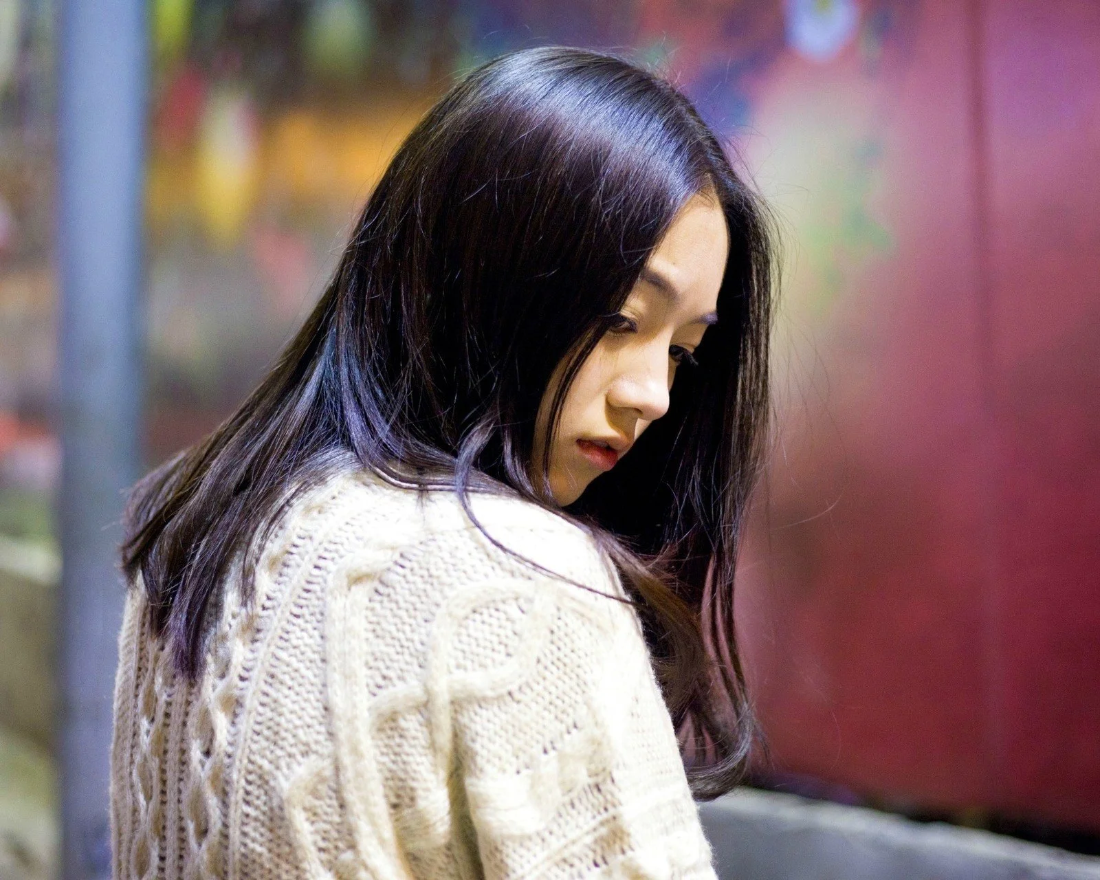 一名长发女性穿着白色针织衫侧身回望。