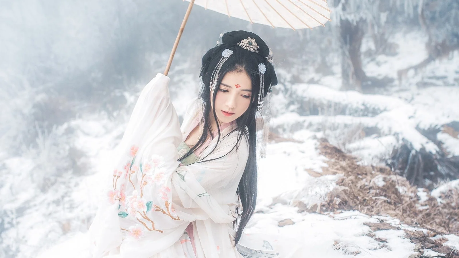 一名身穿白色传统服饰的女子在雪地中撑着伞。