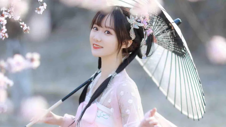 一位身穿浅色传统服饰的女子在花枝与纸伞前微笑。