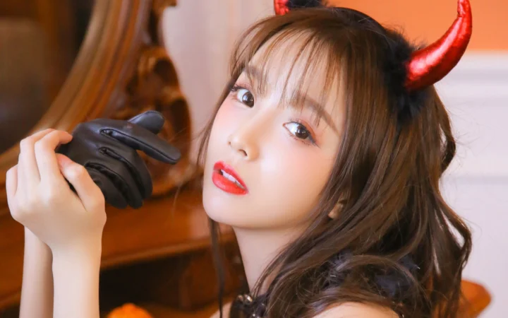 一名戴著紅色角飾、手持黑色手套的女性在室內面對鏡頭。