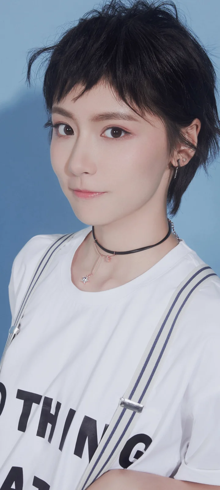 파란색 배경 앞에서 흰색 상의를 입은 짧은 머리 여성이 카메라를 향해 미소 짓고 있다.