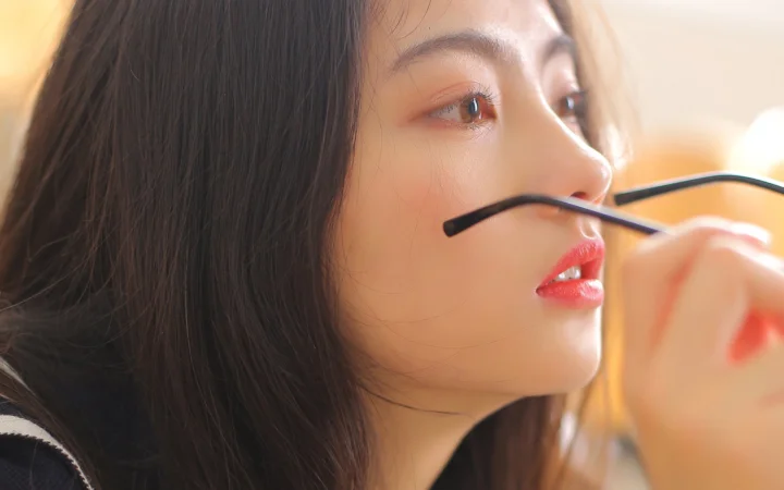 一名成年女性的侧脸近距离特写，她手持黑框眼镜靠近面部。