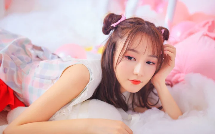 一名女性躺在柔软的白色床品上，周围是粉色背景与蓬松装饰。