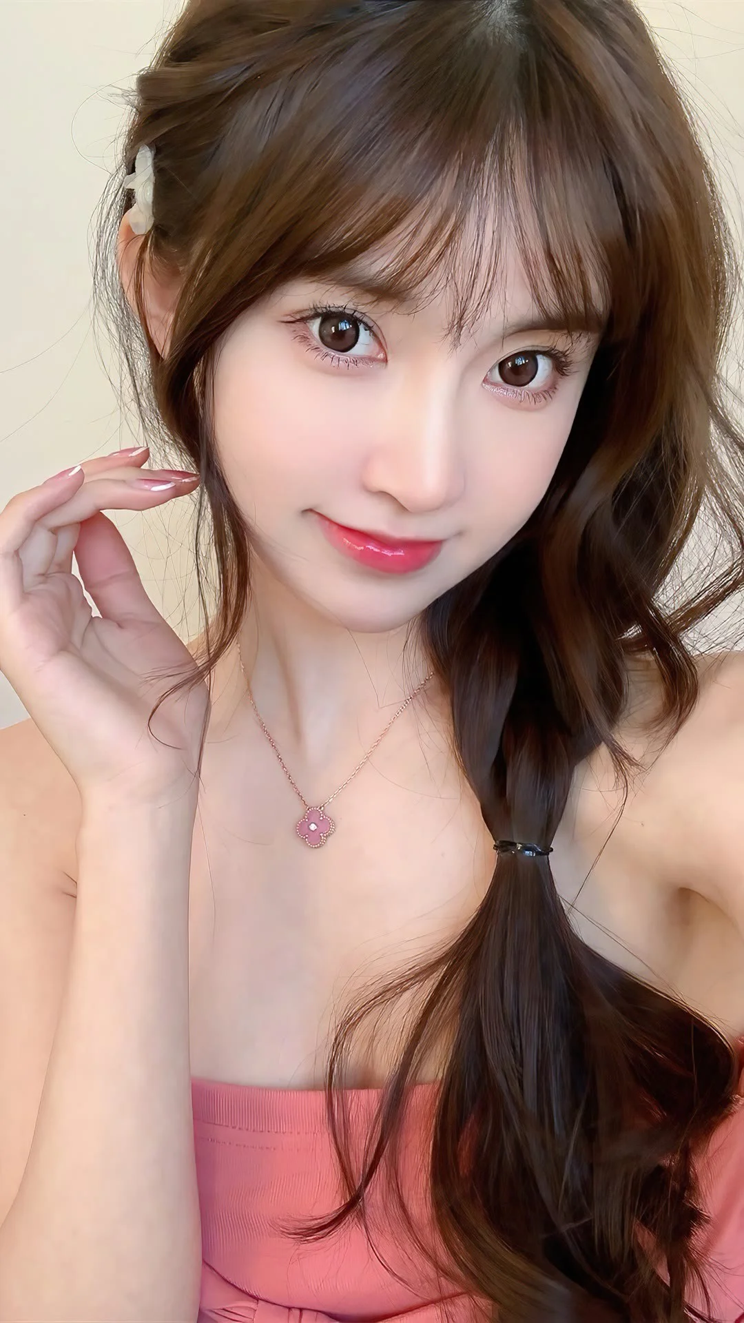 갈색 긴 머리를 옆으로 땋은 여성이 분홍색 상의와 목걸이를 착용하고 카메라를 바라보고 있습니다.