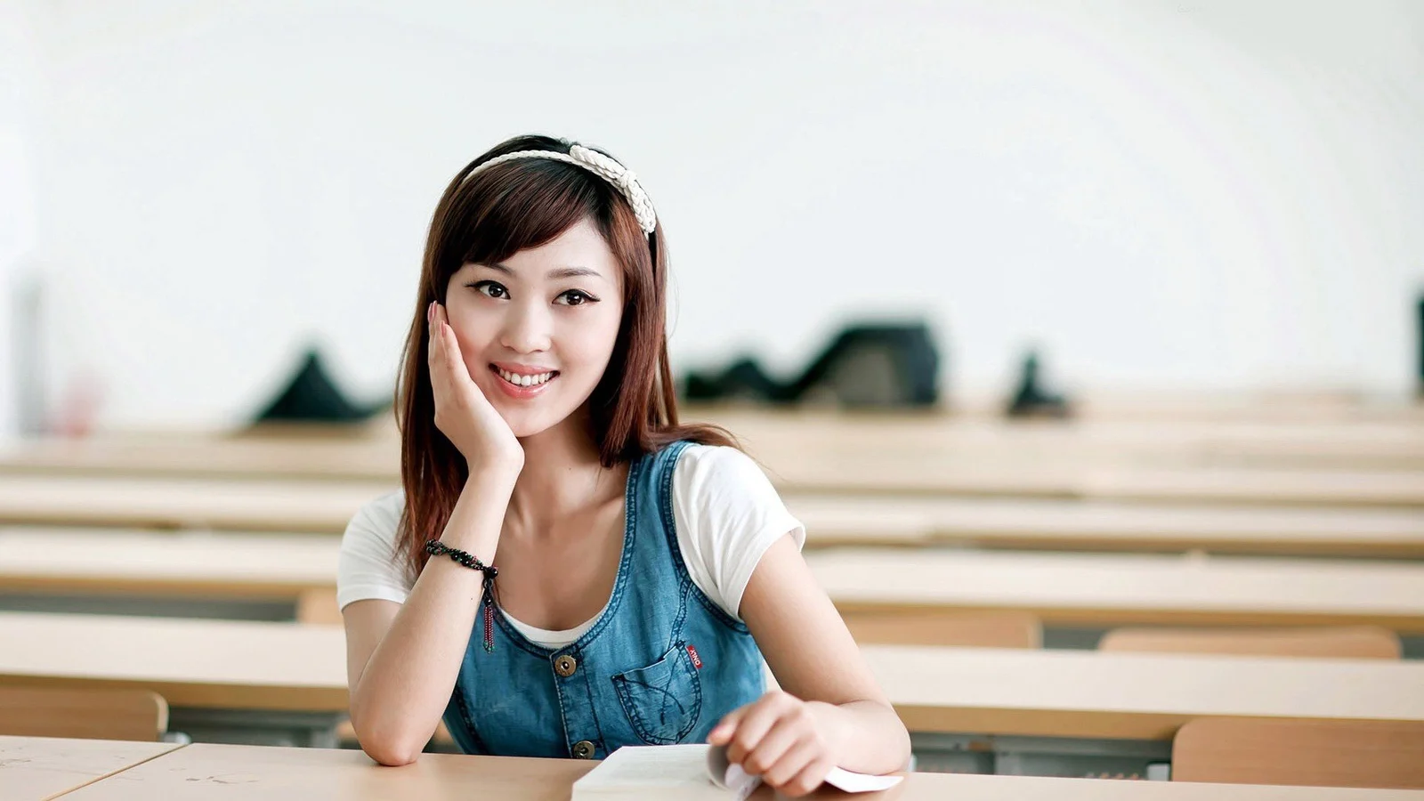 一位面带微笑的成年女士坐在教室课桌前。