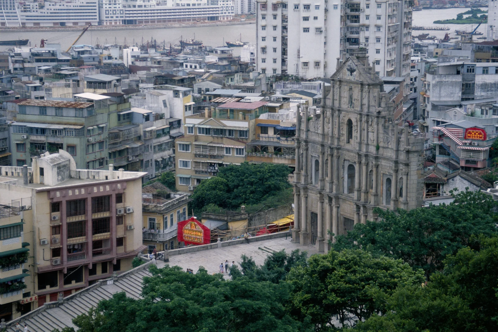 俯瞰澳门密集的城市建筑、绿树与一座历史教堂遗址。