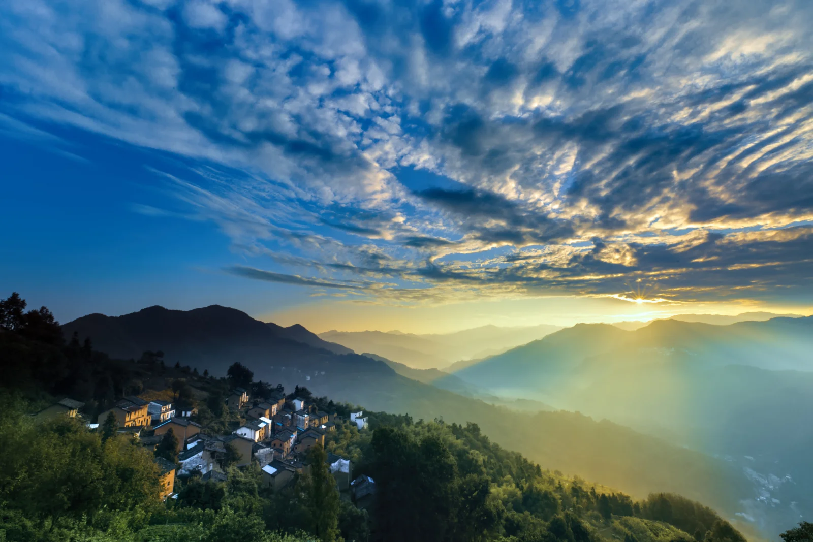 夕阳照耀着层叠群山、云层和山坡上的村庄。