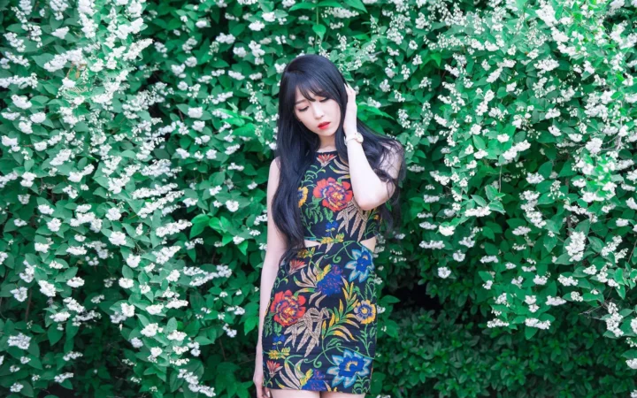 一名长发女子站在盛开白花的绿色灌木前。
