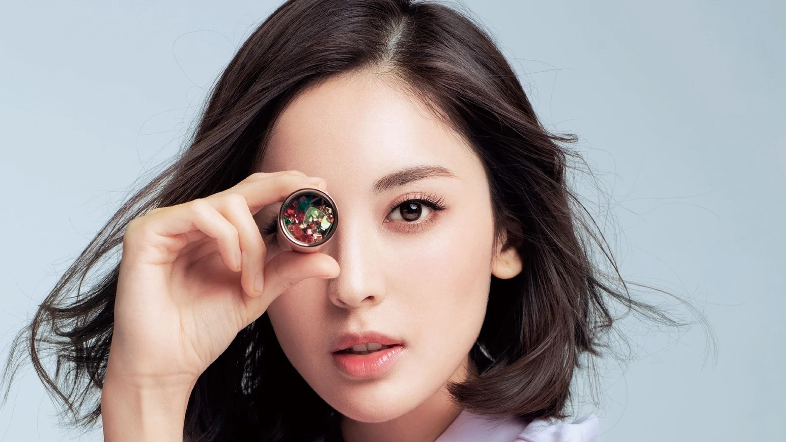 성인 여성이 눈가에 돋보기를 들고 카메라를 바라보는 선명한 스튜디오풍 인물 사진입니다.