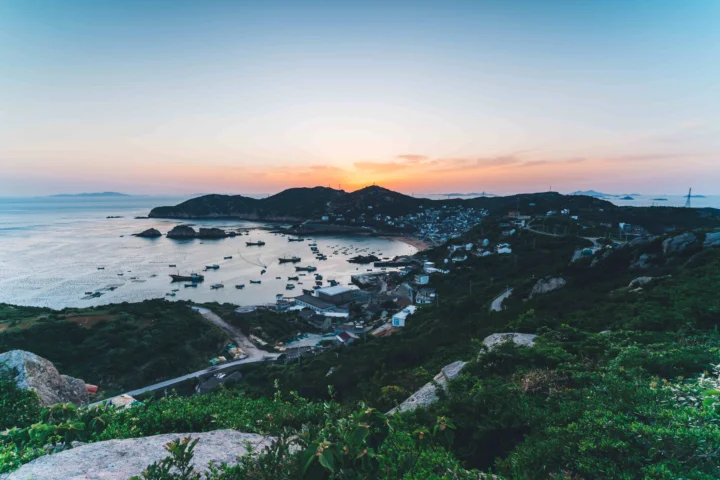 夕阳映照下的海湾、岛屿、沙滩和沿岸植被构成宁静的海岸景色。
