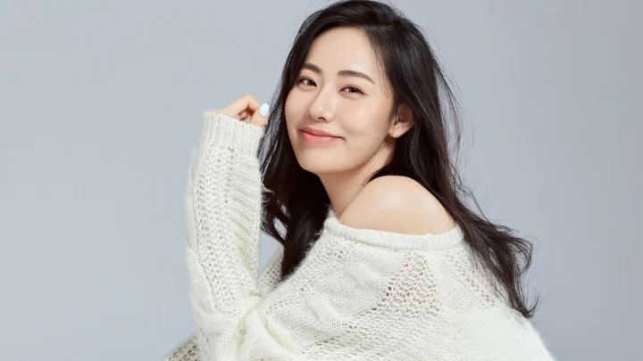 一名成年女性穿着白色宽松针织衫，在浅灰色背景前微笑。