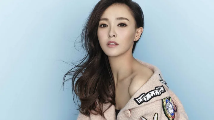 一名长发女性穿着浅色针织衫，在浅蓝色背景前面向镜头。
