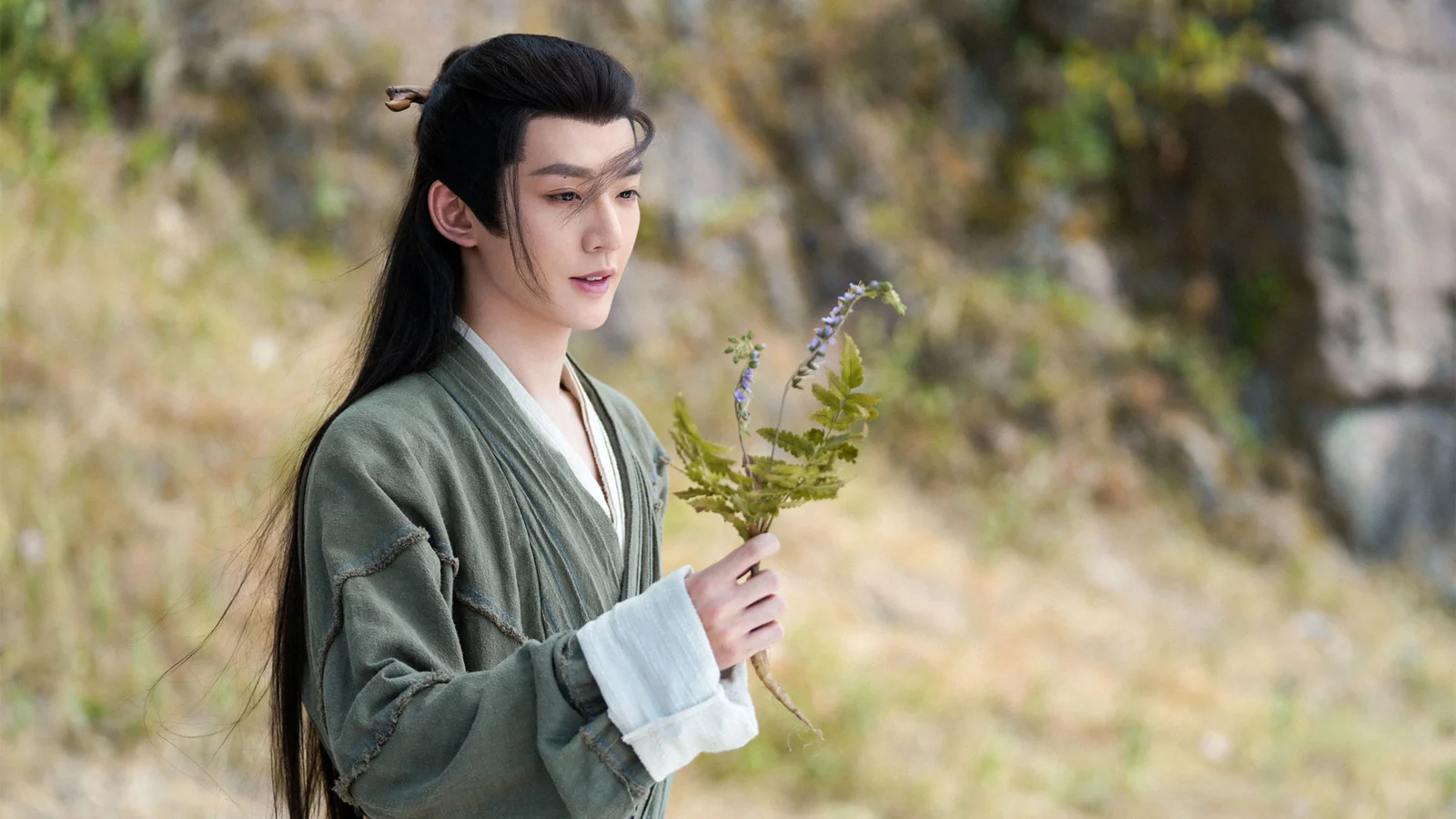一名身穿传统服饰的男子在户外手持一束小花。