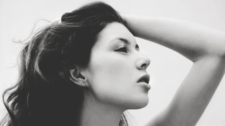 黑白画面中，一名成年女性以侧脸姿态面对右侧，手臂抬至头部上方。