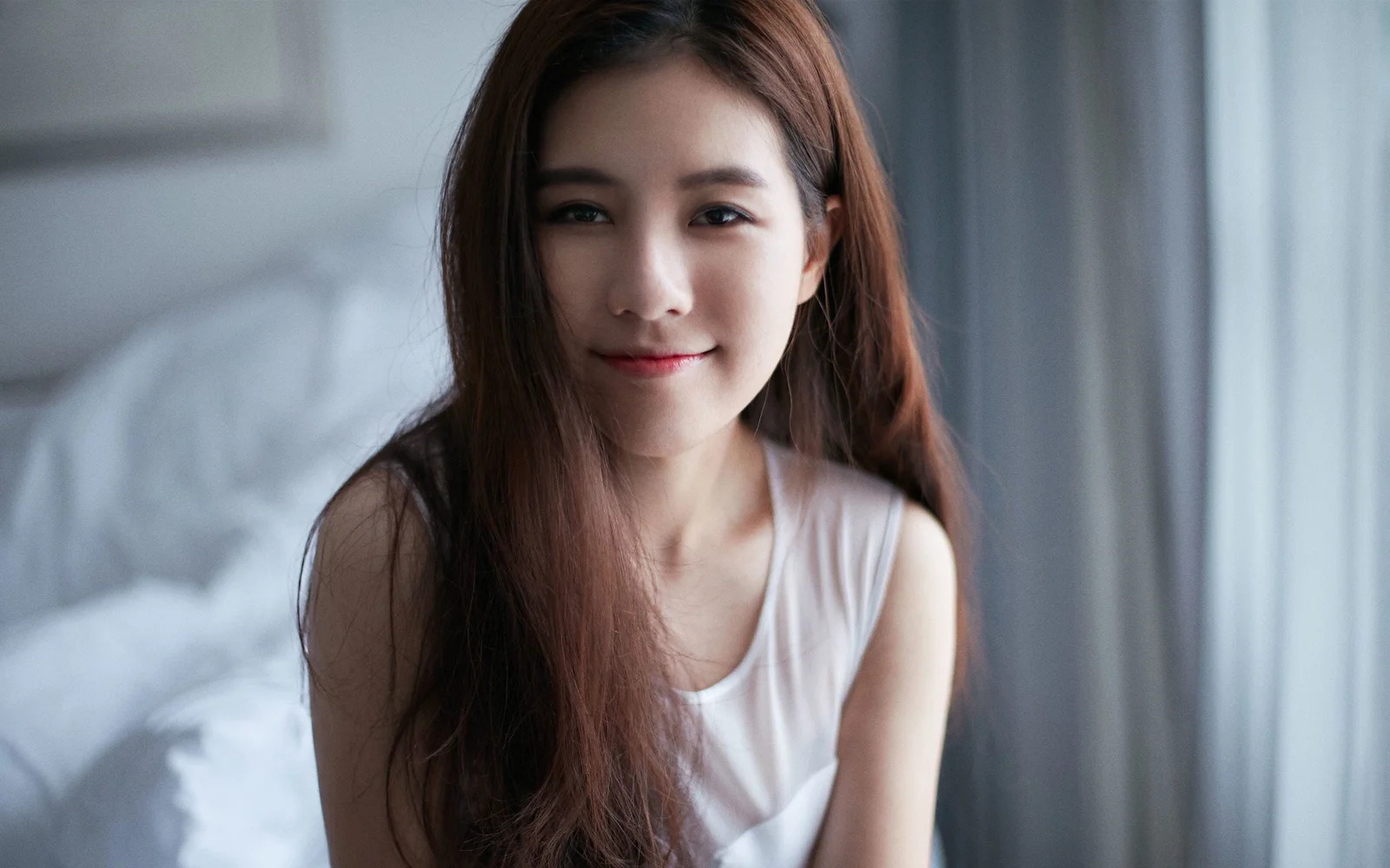 一位長髮女性在室內窗邊微笑面對鏡頭。