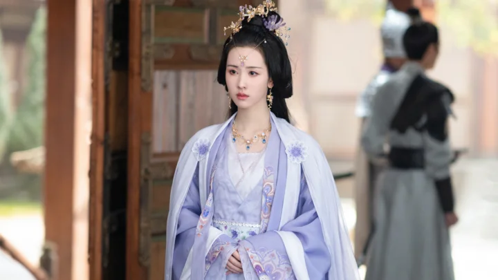 一名身穿淡紫色传统服饰、佩戴华丽头饰的女子站在木门旁。