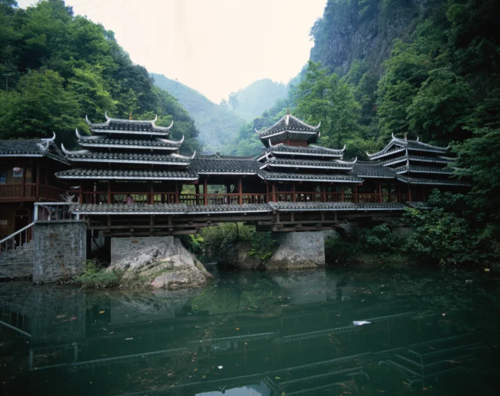 一座带有传统屋檐的古桥横跨清澈池水，周围环绕着茂密森林与青山。