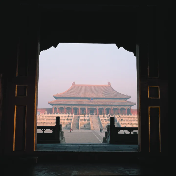 透过深色雕花门洞，可以看到一座红墙琉璃瓦的古代宫殿建筑和宽阔台阶。