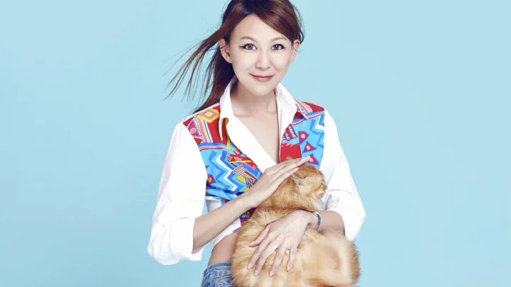 一名女子在浅蓝色背景前抱着一只橘猫。