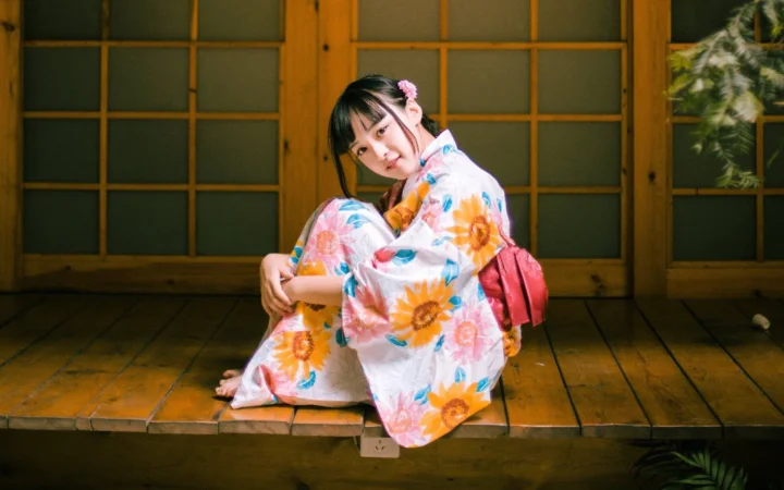 一名身穿花卉浴衣的女子坐在木质地板上，身后是日式木格窗。