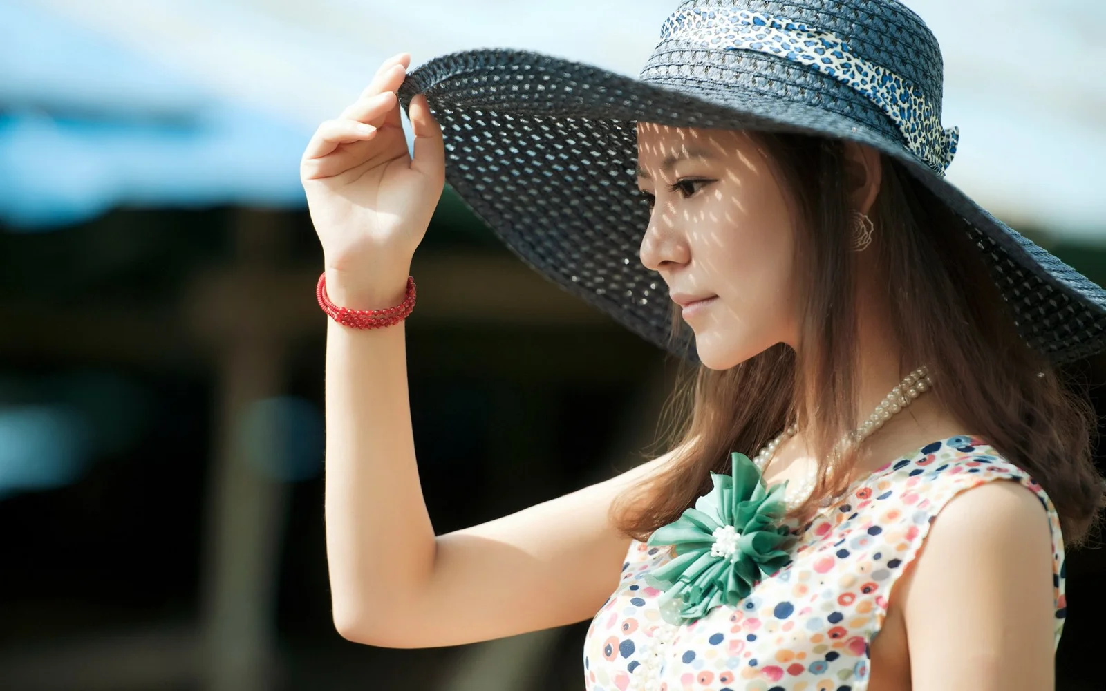 一名戴着宽檐帽、身穿彩色无袖上衣的成年女性在户外侧身望向一侧。