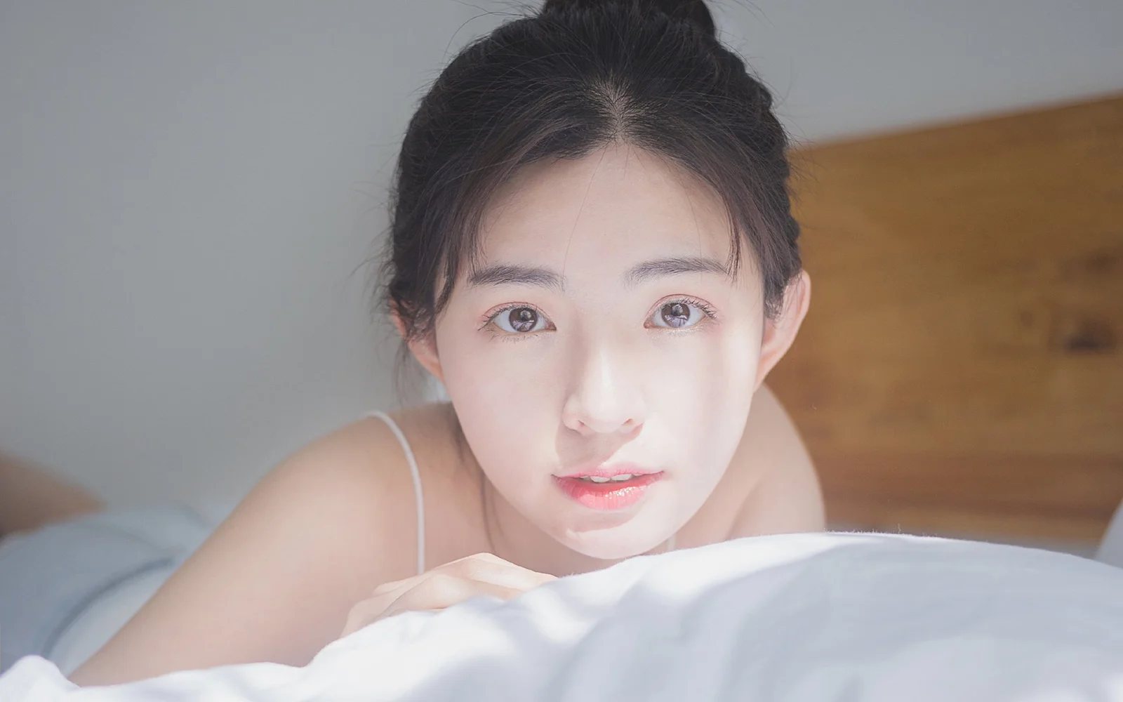 一名女性靠在床上，近距离看向镜头。