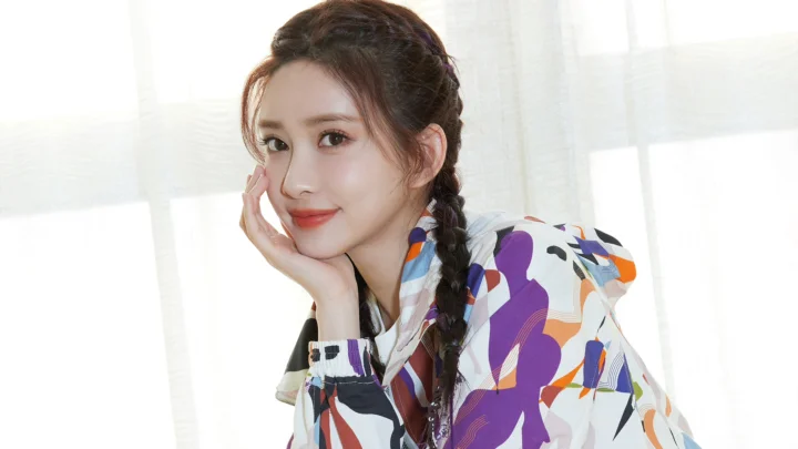 一位留着编发、身穿彩色图案上衣的成年女子在窗边微笑。
