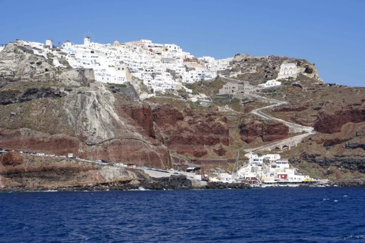 白色建筑群坐落在火山悬崖上方，前景是深蓝色海水。