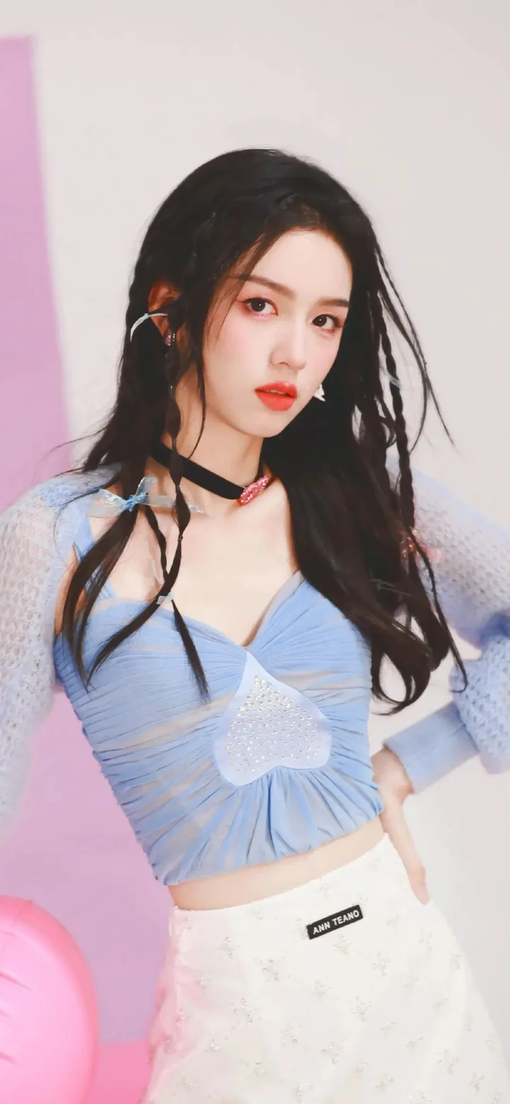 一名长发女性身穿蓝色上衣站在粉色背景前。
